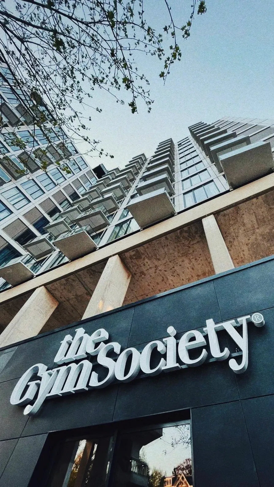 Buitenaanzicht van The Gym Society studio met hoog gebouw op de achtergrond