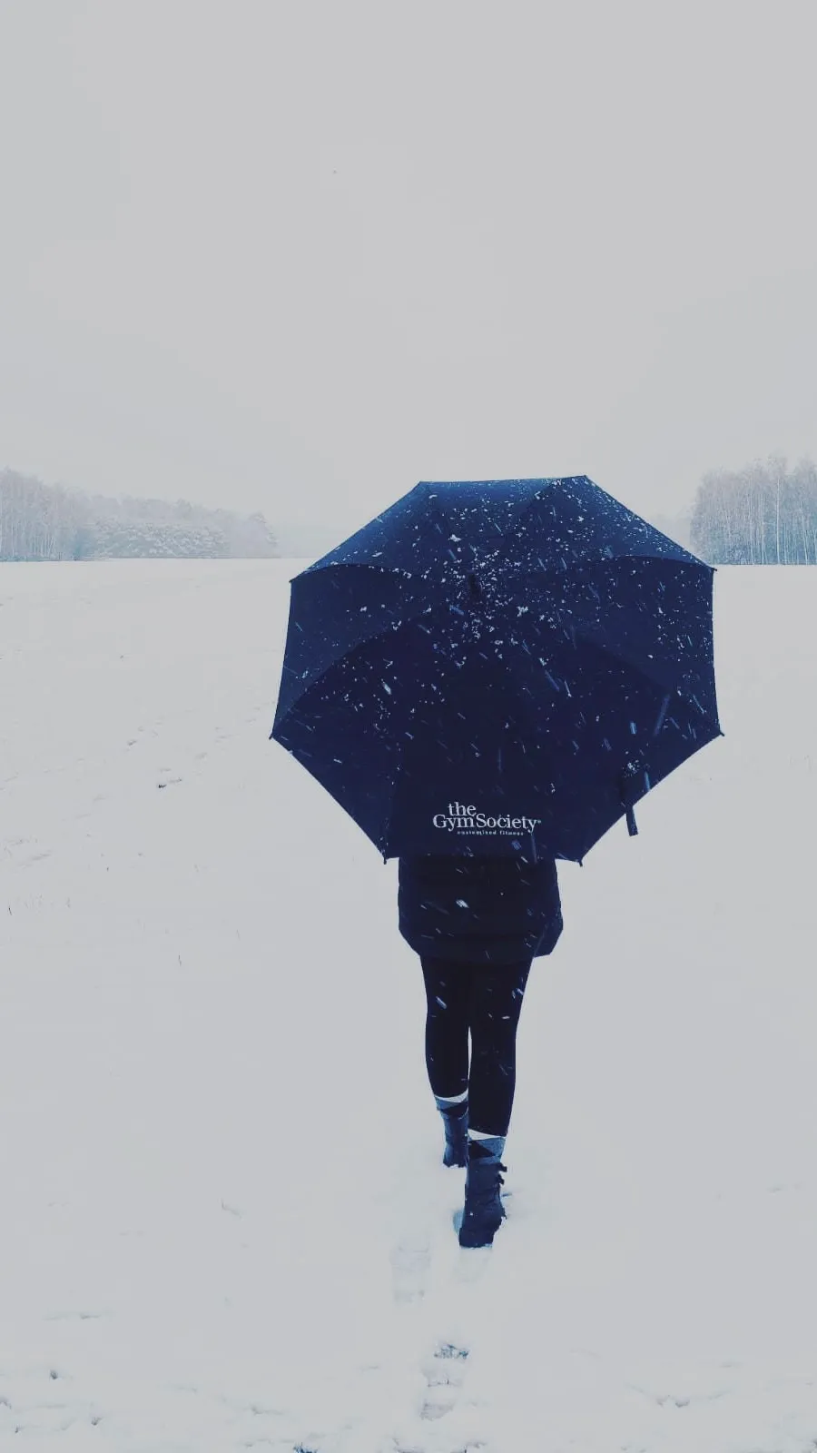 Lid loopt door sneeuwlandschap met The Gym Society paraplu