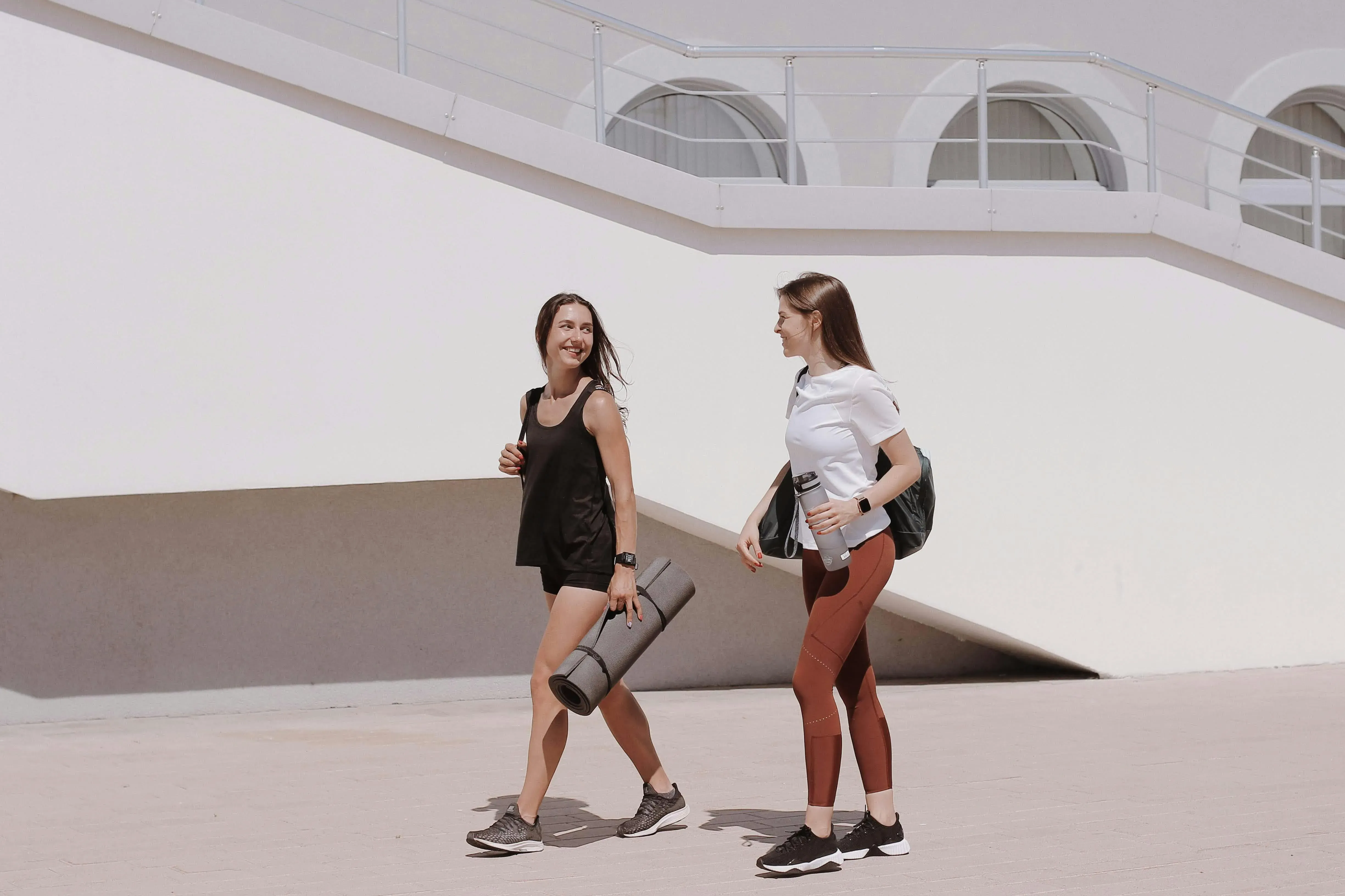 Twee vrouwen lopen samen richting een workout met sportspullen in hun handen