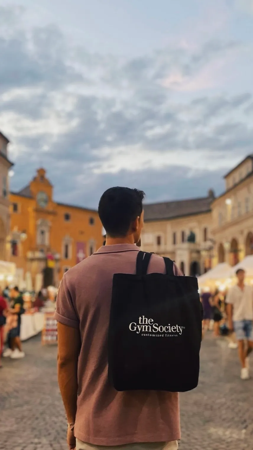 Persoon met The Gym Society totebag op een sfeervol plein in Italië