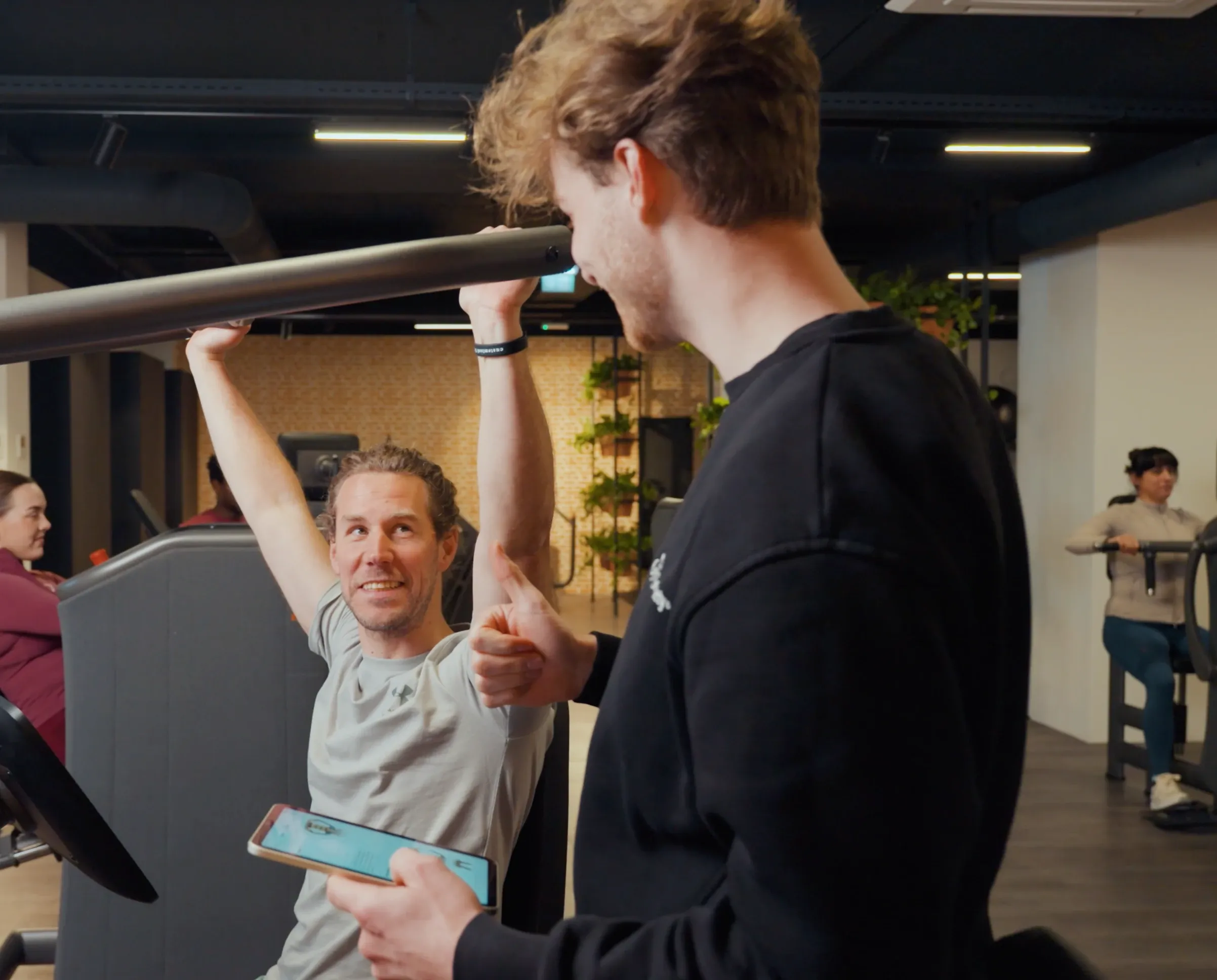 Coach begeleidt een lid tijdens een oefening en geeft een duim omhoog