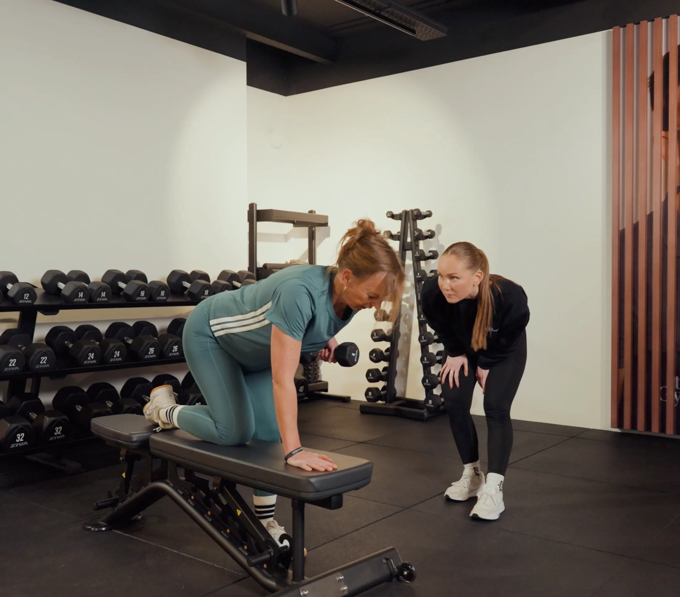 Coach begeleidt een lid tijdens een oefening op de bank met dumbbell