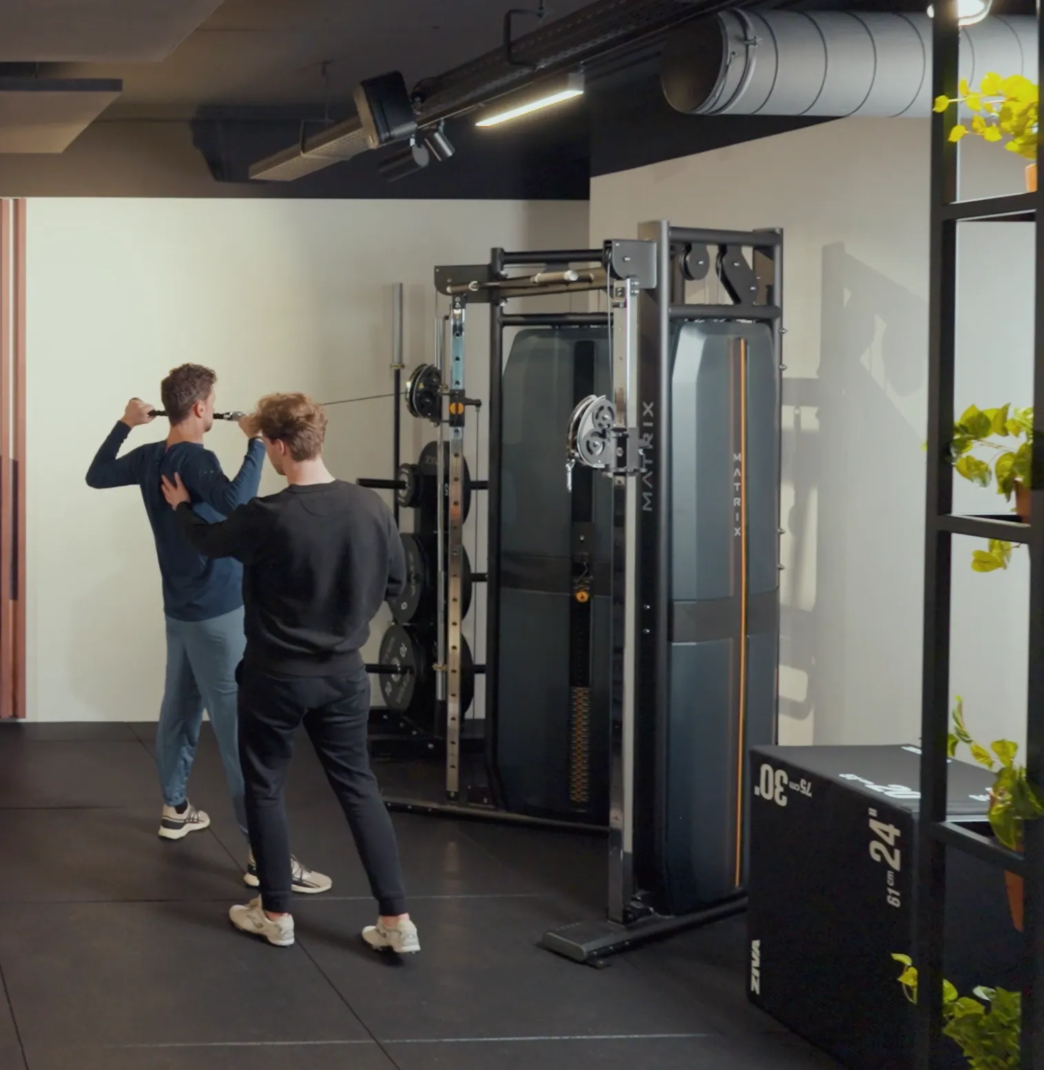 Coach begeleidt een lid tijdens een oefening aan het kabelstation