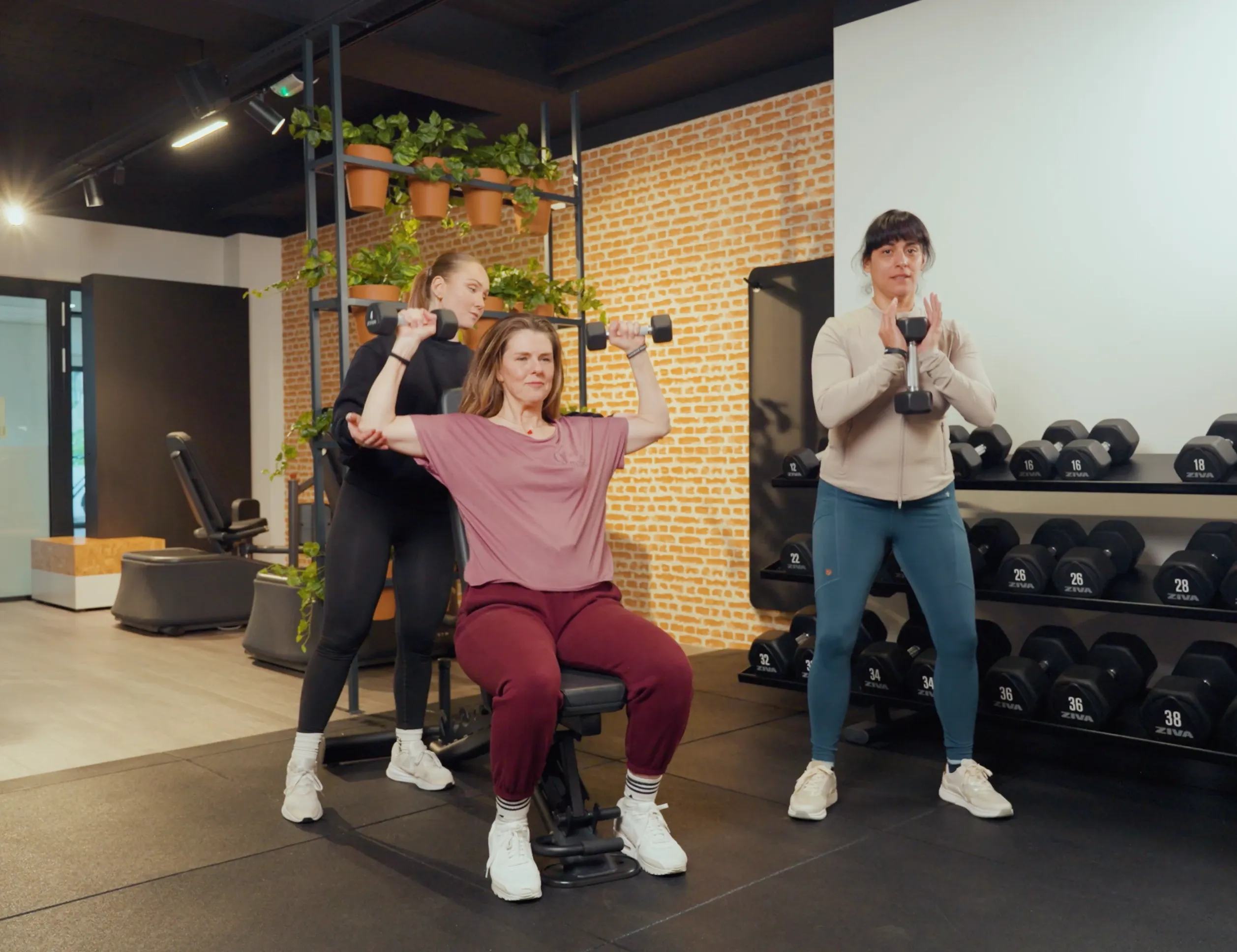 Coach begeleidt twee leden tijdens een duo training met dumbbells