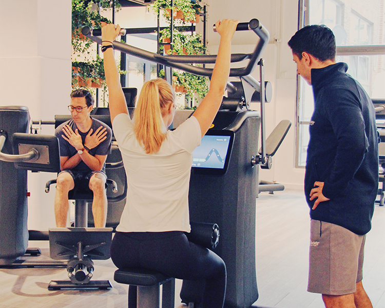 Een mannelijke Lifestyle Coach van The Gym Society die een lid begeleidt op een toestel