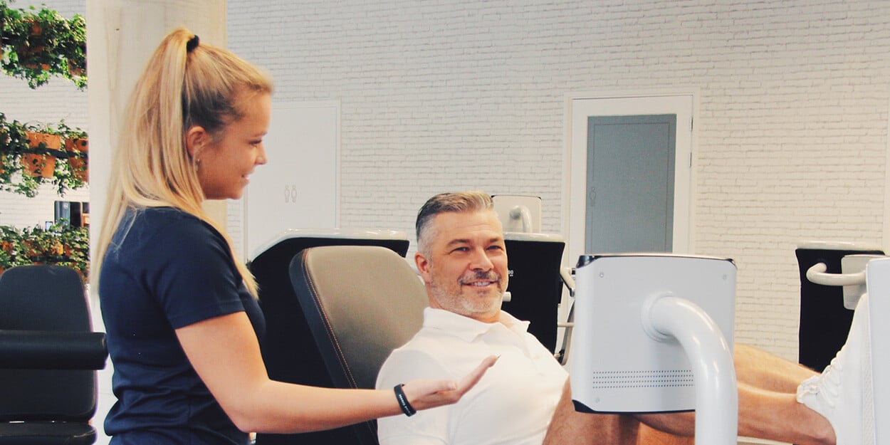 Een vrouwelijke Lifestyle Coach van The Gym Society die een lid begeleidt op een toestel